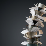 Bodegón elegante con una torre inestable de tazas de café expreso sobre una base de recibos de papel.